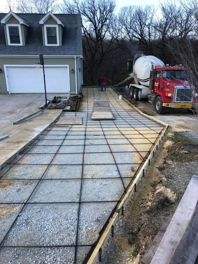 Concrete driveway being poured; red cement truck, rebar grid, residential setting.