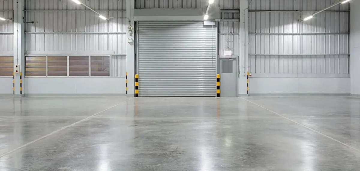 Interior of an empty warehouse with a large closed metal door. Concrete floor. Bright lighting.