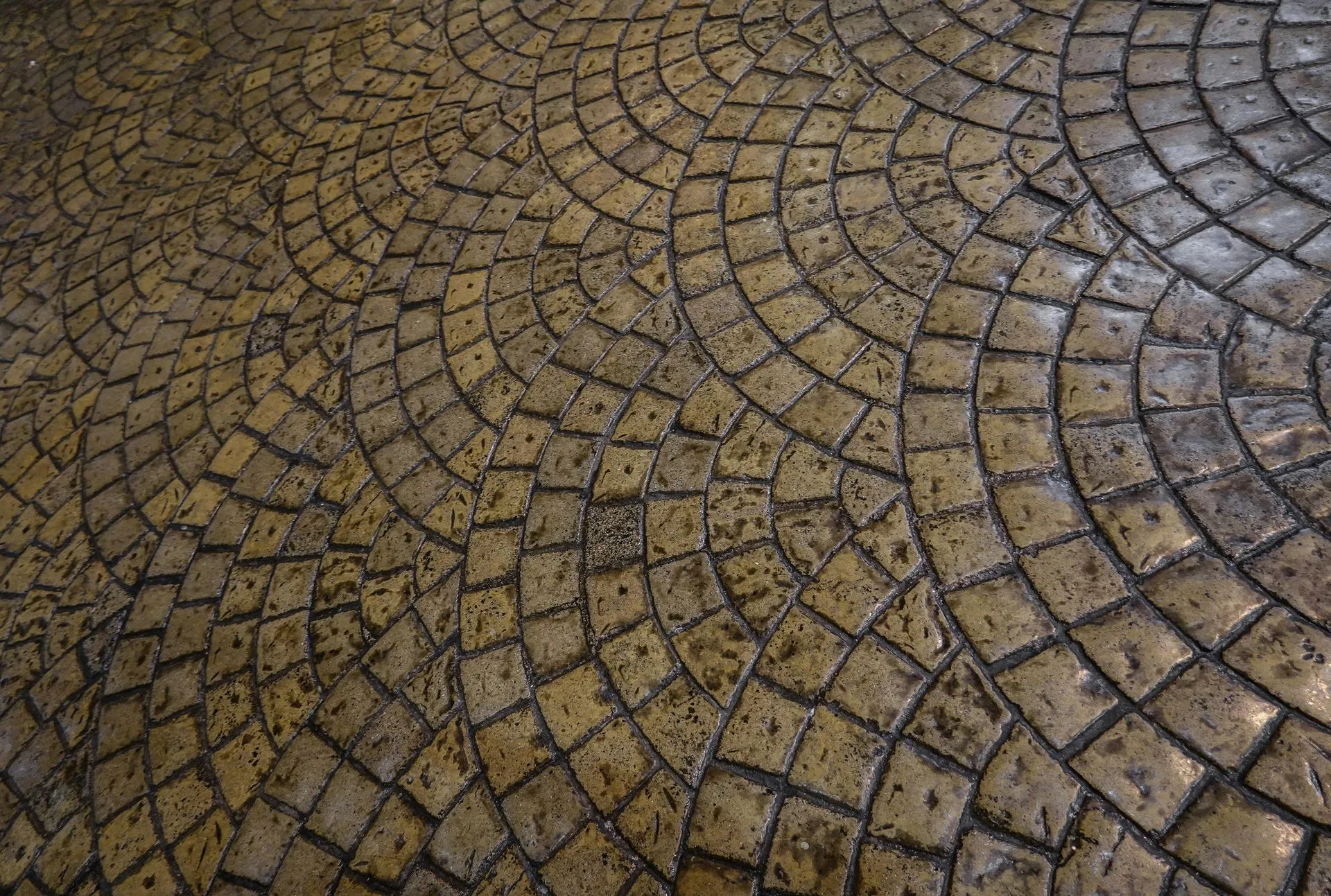 Curved pattern of wet cobblestone paving in brown and gray tones